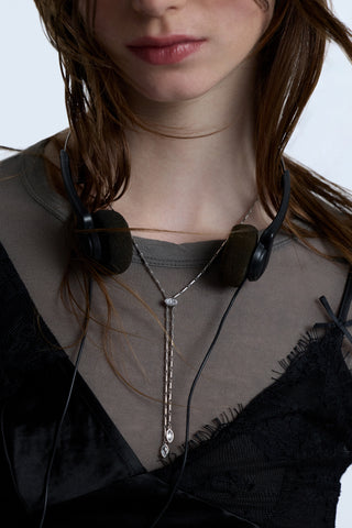 CLOSE UP OF A MODEL’S CHEST AS SHE WEARS A BLACK LACE CAMI LAYERED OVER A GRAY TOP, WITH EARPHONES AROUND HER NECK AND THE SUPERNOVA LARIAT NECKLACE ON