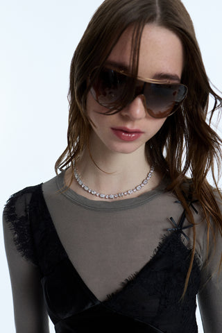 A MODEL WEARING SUNGLASSES, A GRAY LONG SLEEVE SHIRT, A BLACK LACE CAMI, AND THE SUPERNOVA COLLAR NECKLACE