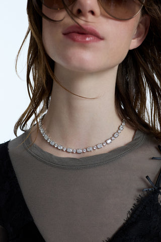 CLOSE UP OF A MODEL’S NECK AS SHE WEARS SUNGLASSES, A GRAY SHIRT, AND A BLACK LACE CAMI WITH THE SUPERNOVA COLLAR NECKLACE LAYERED OVER TOP