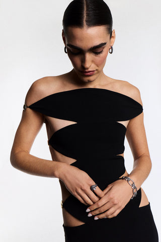 A MODEL STANDING AND LOOKING DOWN WITH HER HANDS IN FRONT OF HER, AS SHE WEARS A BLACK DRESS, THE TURN UP THE VOLUME OVAL LINK LINE BRACELET, AND THE MATCHING RING
