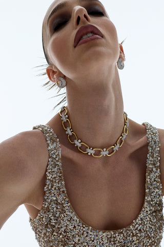 A MODEL WITH HER EYES CLOSED AND HER NECK EXTENDED, WEARING A GOLD SPARKLY DRESS AND THE TURN UP THE VOLUME LINK ALL AROUND NECKLACE