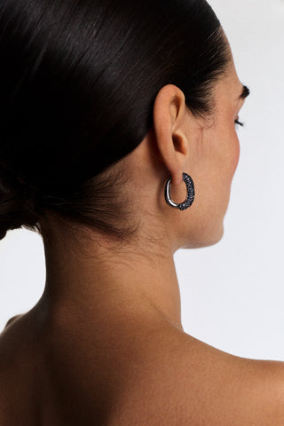 VIEW OF THE BACK OF A MODEL’S HEAD TURNED SLIGHTLY TO THE SIDE, AS SHE WEARS A SLICK BACK BUN AND THE TURN UP THE VOLUME OVAL HOOP EARRINGS