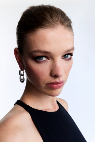 MODEL LOOKING AT THE CAMERA WEARING A HIGH-NECK BLACK TOP AND THE BLACK TURN UP THE VOLUME DOORKNOCKER EARRINGS