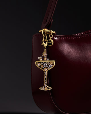 Champagne Glass Bag Charm with cubic zirconia and pearl accents on a burgundy handbag against a dark background.