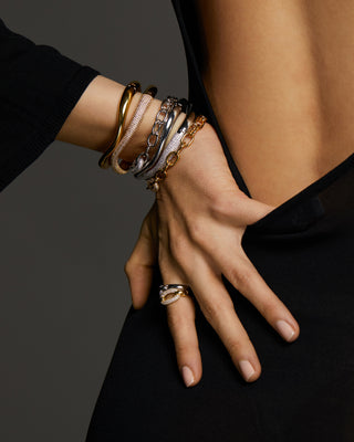 Close up image of model with her hand on her hip. She's wearing a stack of six bracelets in silver and gold plating and two rings. 
