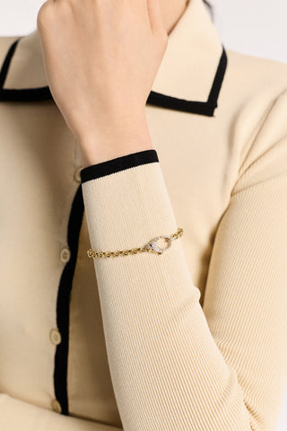 CLOSE UP OF A MODEL RAISING HER WRIST, WEARING AN IVORY SHIRT AND THE GEMINI PAVE CLASP LINE BRACELET IN GOLD PLATING OVER HER SLEEVE