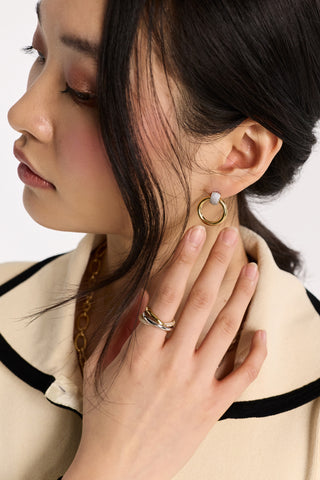 CLOSE UP OF A MODEL’S EAR WITH HER HAIR FRAMING HER FACE AND HER HAND LIFTED UP, WEARING THE GEMINI DOOR KNOCKER EARRINGS AND GEMINI TRIO RING