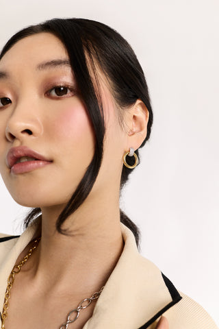 CLOSE-UP OF A MODEL LOOKING AT THE CAMERA WEARING GEMINI DOOR KNOCKER EARRINGS WITH A STRAND OF HAIR FRAMING HER FACE