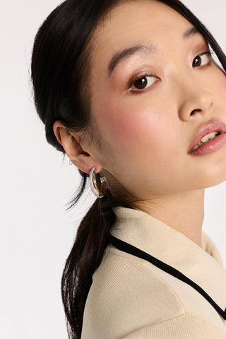 CLOSE UP OF A MODEL’S PROFILE WITH HER HAIR IN A PONYTAIL BEHIND HER EAR AND WEARING THE GEMINI TWO TONE C HOOP EARRINGS