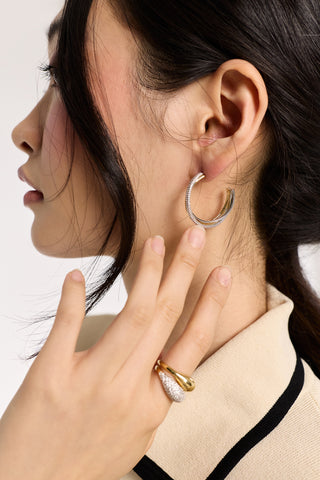CLOSE UP OF A MODEL’S SIDE PROFILE AND HER HAND LIFTED TO HER EAR, WEARING THE GEMINI TWO TONE C HOOP EARRINGS AS HER HAIR FRAMES HER FACE