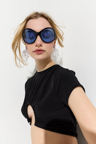 A MODEL IN A BLACK TOP WITH HER HAIR BLOWING BEHIND HER, WEARING BLUE SUNGLASSES AND THE MOJITO LARGE CHANDELIER EARRINGS
