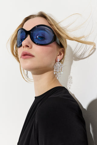 CLOSE UP OF A MODEL WITH HER HAIR BLOWING BEHIND HER, WEARING BLUE SUNGLASSES AND THE MOJITO LARGE CHANDELIER EARRINGS