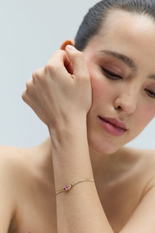 CLOSE UP OF A MODEL LOOKING DOWN WITH HER WRIST LIFTED UP TO HER FACE, WEARING THE DELANCEY PINK PEAR LINE BRACELET
