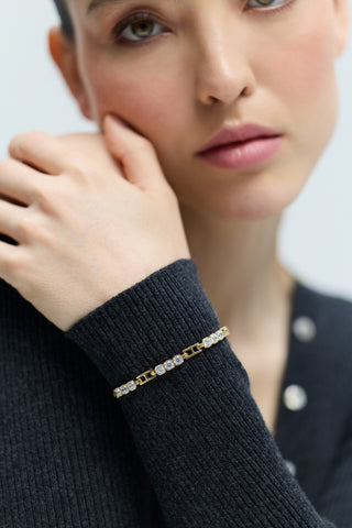 CLOSE UP OF A MODEL LOOKING AT THE CAMERA WITH HER HAND LIFTED UP TO HER SHOULDER, WEARING THE DELANCEY LINE BRACELET LAYERED OVER A GRAY SWEATER