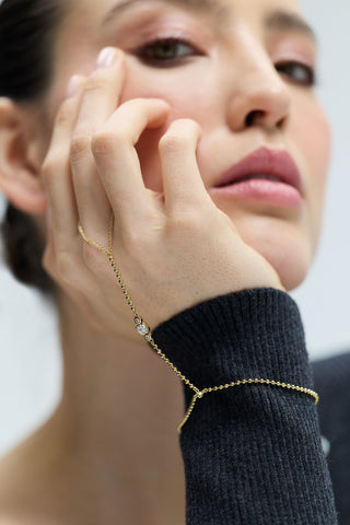 CLOSE-UP OF A MODEL RESTING HER CHIN ON HER HAND, WEARING A GRAY SWEATER AND THE DELANCEY HAND CHAIN BRACELET