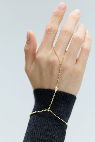 A HAND RAISED, WEARING THE DELANCEY HAND CHAIN BRACELET WITH A GRAY SWEATER SLEEVE VISIBLE.