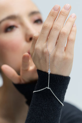 CLOSE-UP OF A MODEL'S HAND IN FOCUS, WEARING THE DELANCEY HAND CHAIN BRACELET WITH GRAY SWEATER SLEEVES VISIBLE