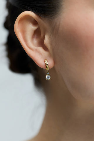 CLOSE UP OF A MODEL’S EAR, WEARING THE DELANCEY SMALL CHARM HOOP EARRINGS IN GOLD PLATING