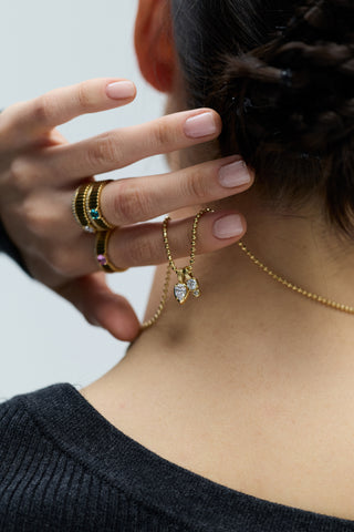 BACK VIEW OF A MODEL WITH A TWISTED BRAID UPDO, HOLDING THE DELANCEY CHARM PENDANT NECKLACE AT THE BACK OF HER NECK, WHILE WEARING DELANCEY SOLITAIRE RINGS ON HER FINGERS