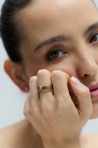 CLOSE UP OF A MODEL LOOKING AT THE CAMERA, RESTING HER CHIN ON HER CURLED HAND, WITH HER HAND IN FOCUS WEARING THE DELANCEY PINK SOLITAIRE RING