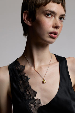  A MODEL WITH SHORT HAIR LOOKING UP TO THE SIDE AS SHE WEARS A BLACK LACE TOP AND NADRI’S MACARON YELLOW CUSHION CZ PENDANT IN RHODIUM PLATING