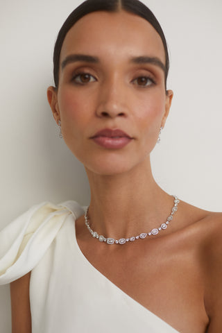 IMAGE OF A BRIDE WEARING OUR RADIANT FULL COLLAR CZ NECKLACE WITH MATCHING DROP EARRINGS.  HER WHITE DRESS IS OFF THE SHOULDER WITH A BOW DETAIL AND HER HAIR IS PULLED BACK SLEEKLY AS SHE LOOKS DIRECTLY INTO THE CAMERA.