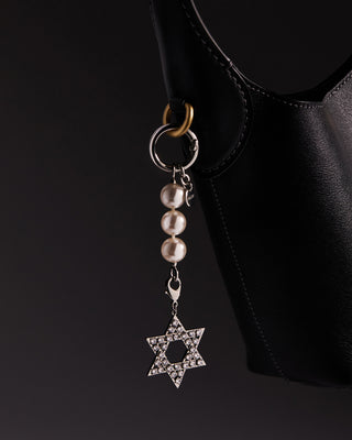 Star of David bag charm with a pearls chain on a black handbag against a dark background.