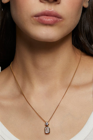Woman wearing a delicate necklace with a clear pendant on a plain background