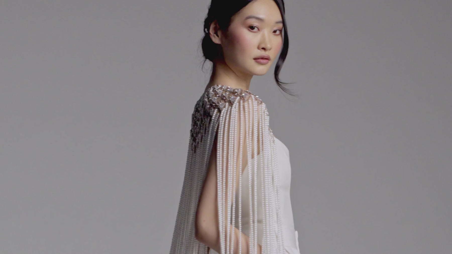 Model wearing a white suit with Nadri's Pearl and CZ cape. She is elegantly moving and showing off the cape from every angle.
