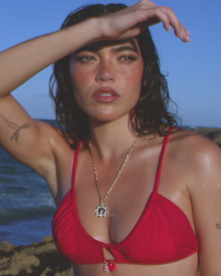 Video of model in a red bikini wearing the GlobeTrotter Compass pendant while on a rocky beach.