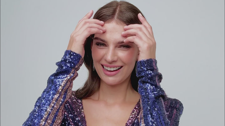 Model in blue and purple sequin dress trying on earrings from our Starlet collection.