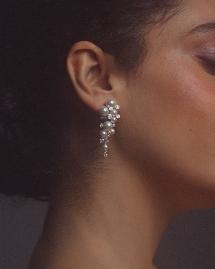 Video of model wearing Nadri's Under the Sea pearl cluster earrings and bracelet.  Her dark hair is pulled back and she is dancing and twirling in a voluminous black and white ostrich feather jacket and white gown.