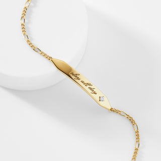A gold ID bracelet that says "slay all day" with a cubic zirconia stone