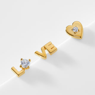 Gold stud earrings that spell out "LO-VE" and a gold heart stud earring with a CZ stone